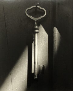 Schwarzweißfotografie eines Schlüssels, der an einem Haken hängt. Das Bild enthält starke Kontraste zwischen Licht und Schatten.